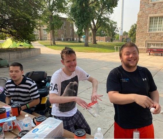Three smiling campers prepare to boil their egg breakfast in baggies