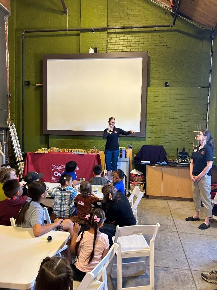 children and their families watch the ASL storyteller who stands in front of a large screen