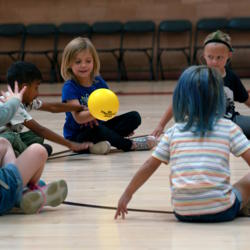 A girl holds a yellow ball and smiles, while students around her wait for the ball to come to them.