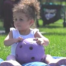 Girl sitting in grass playing with purple ball