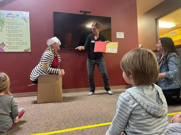 ASL storyteller holds a book while another lady acts out the story and children watch
