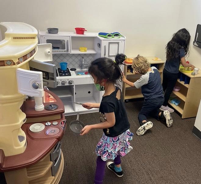 Two young girls and a young boy play in a pretend kitchen