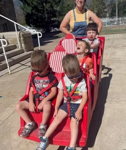 Four preschool students sit in the six-seated cart, being pushed by their teacher on a sunny day!