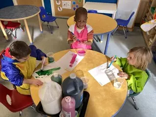 Three students paint at a classroom table