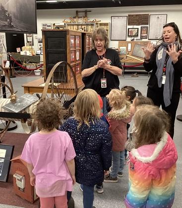 Female volunteer talks with six preschool students about the 1950 fire, while interpreter signs