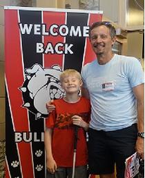 a boy with a cane and his dad pose next to the Welcome Back Bulldogs banner