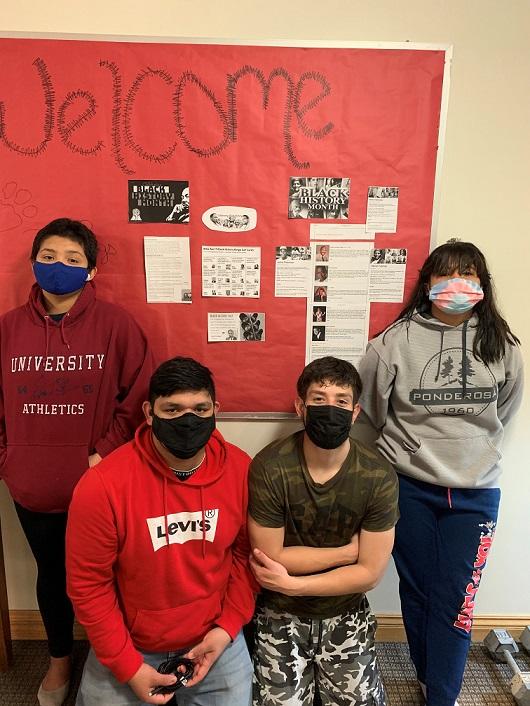 Four students stand in front of a bulletin board about Black History Month