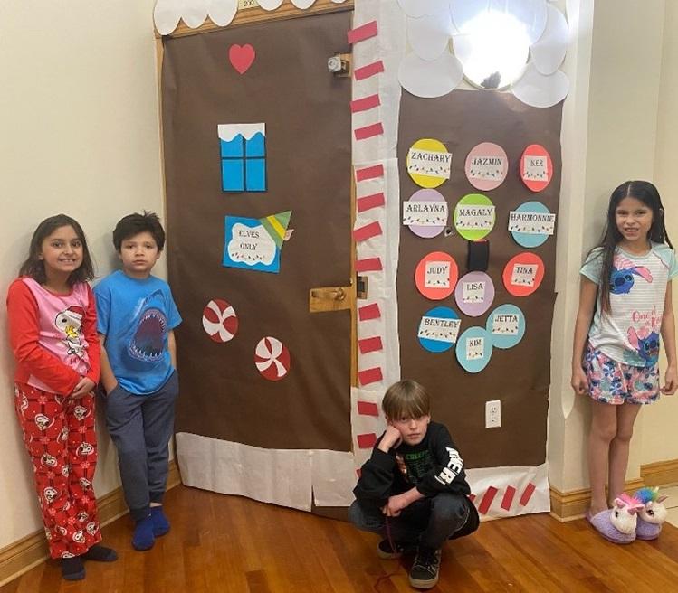 Four kids in front of their gingerbread house entrance to their dorm