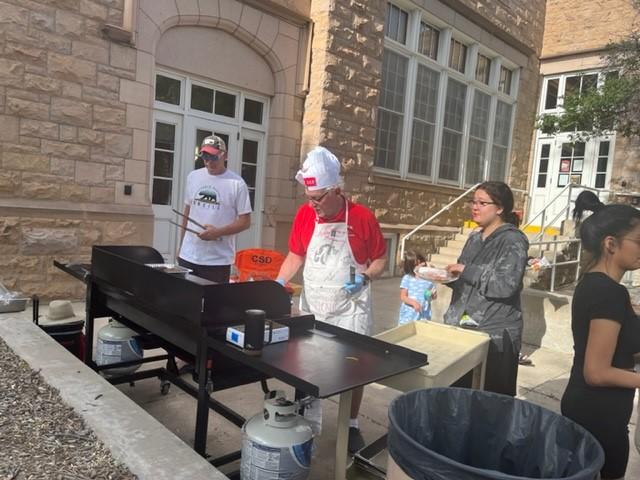 Three people stand behind the BBQs cooking