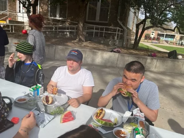 Three students eat at an outdoor table