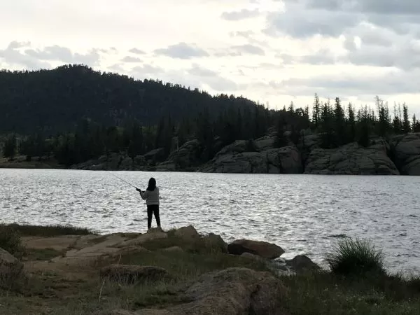 Student fishing on camping trip at a lake with a natural mountain landscape on the other side of the lake