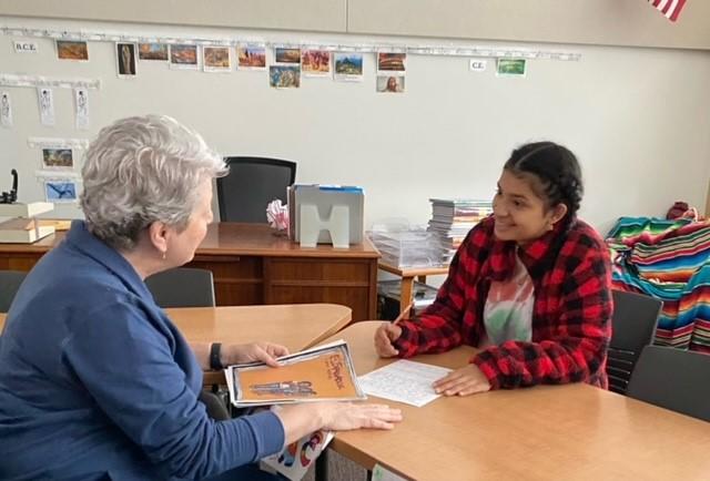 Female teacher and student work together across a table in the classroom.
