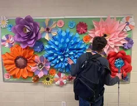 student explores a tactile bulletin board with gigantic multi-colored and multi-shaped flowers.