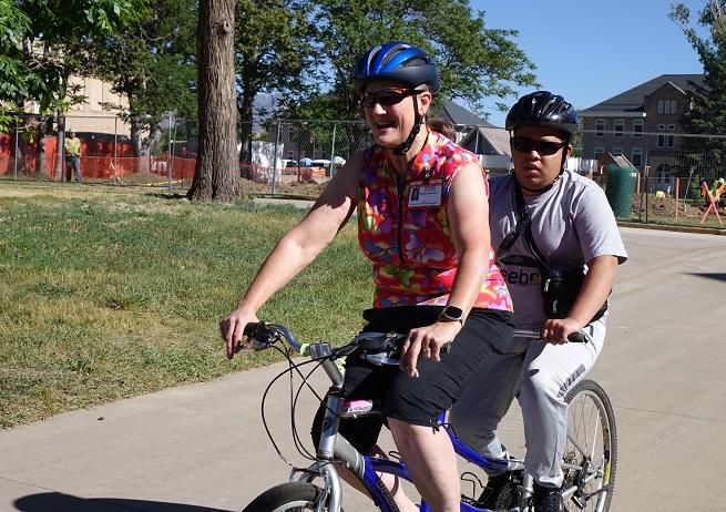 Lady and student pedal by on a tandem bicycle