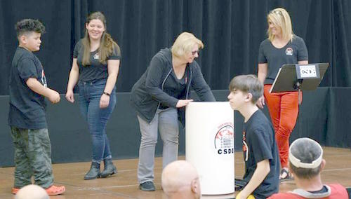 A group of students and staff on the stage putting items into the time capsule