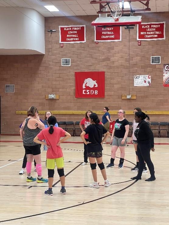 A group of CSDB volleyball players standing in a circle on the gym floor.