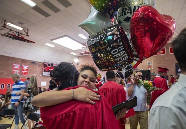 Male graduate is hugged by a relative who holds a balloon bouquet