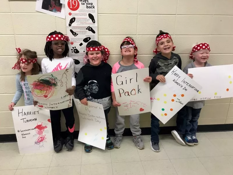 elementary students standing against a wall with women's day signs