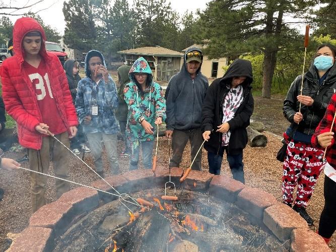 Students roast hotdogs over a campfire