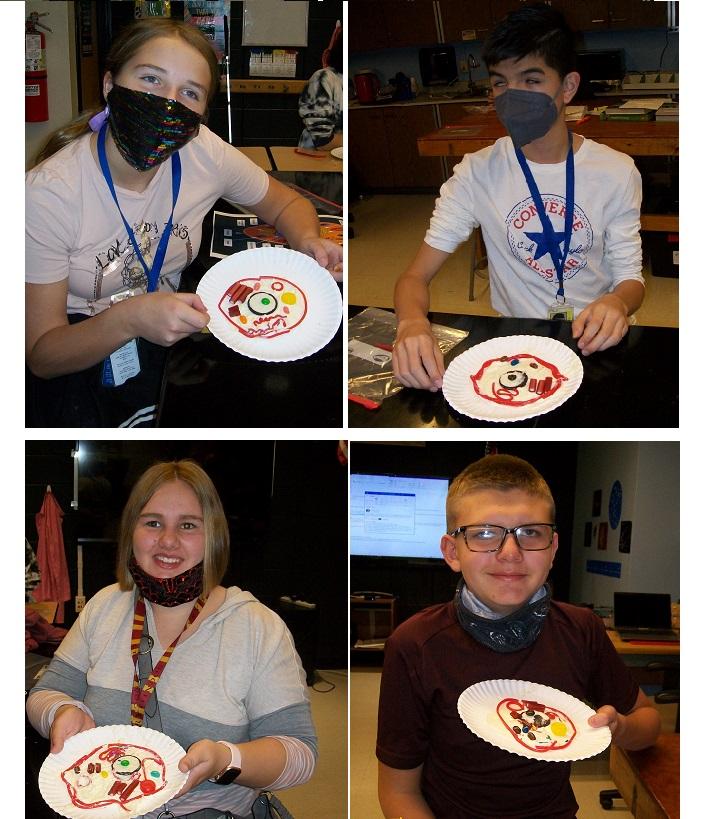 Four students show off their candy cell models, created with candy, on paper plates