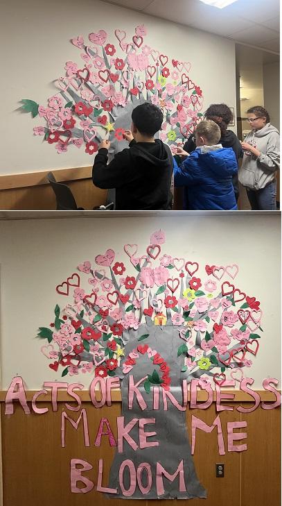 four students create a wall paper display of the kindness tree "Acts of Kindness Make Me Bloom"