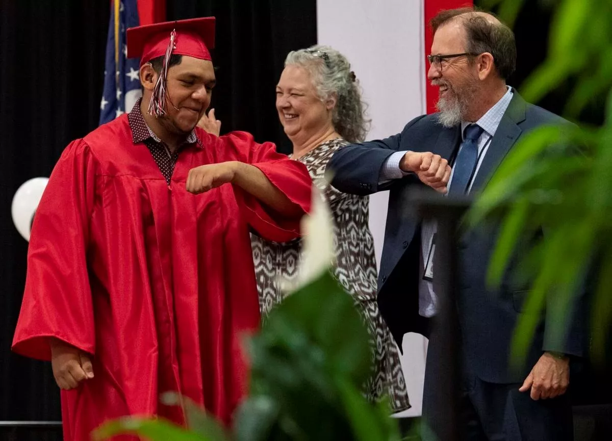 One graduate gives a Board member an elbow bump on stage