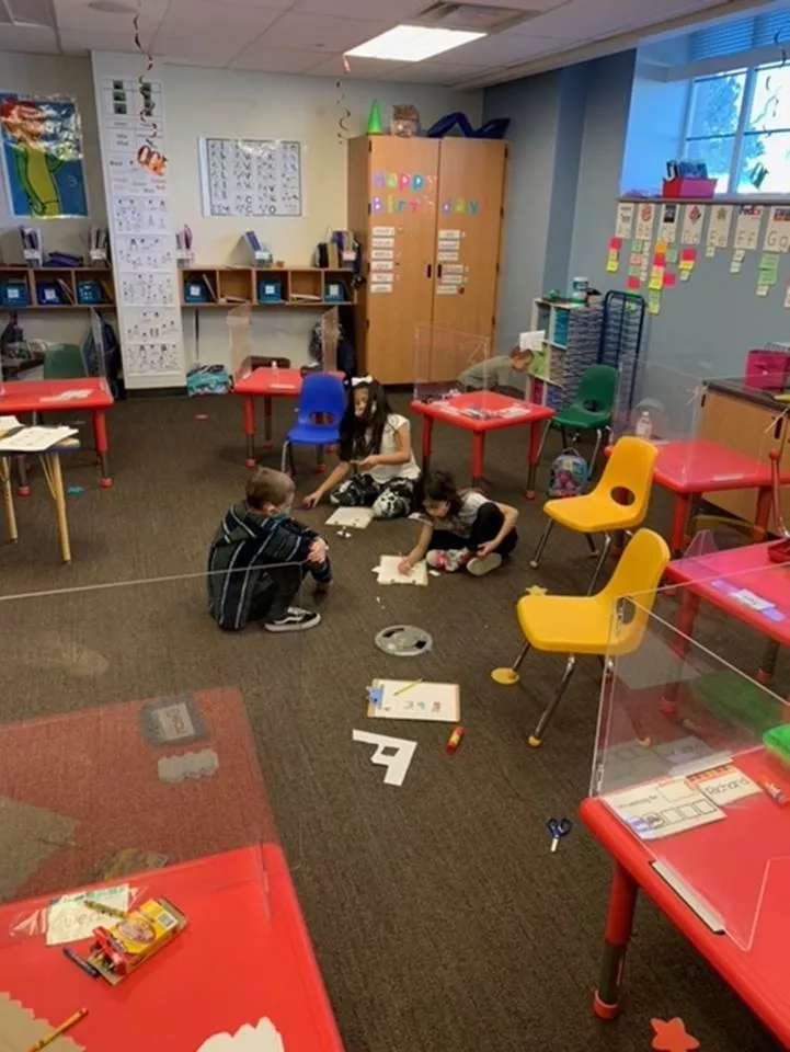 Two girls and one boy work on a project on the classroom floor