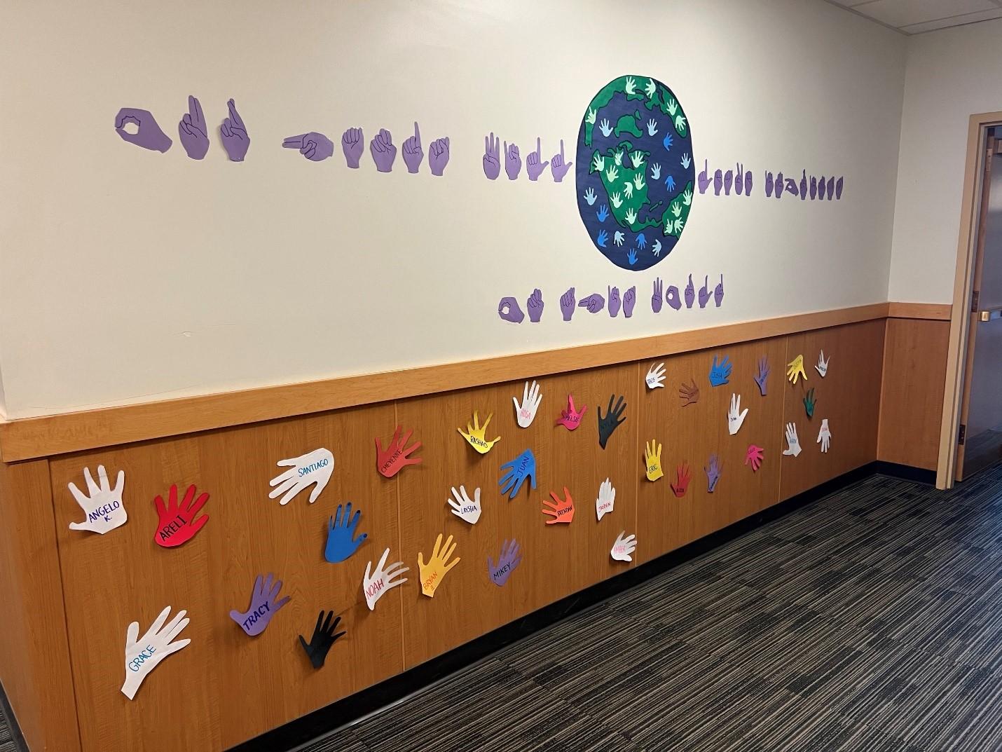 On the wall there are student and teacher hand shapes in multiple colors of paper.