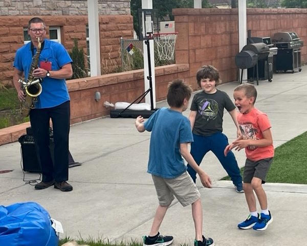 three students dance to the music of the saxophone during an outdoor concert.