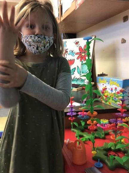 Child holds up a hand while flowers are on the background painting