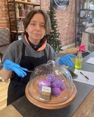 Female Deaf Bridges to Life student is standing behind a display of bath bombs that she assembled for her work study site: Rocky Mountain Soap Factory.