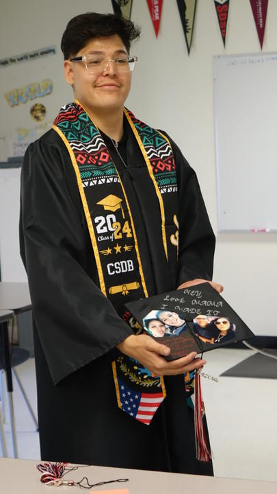 Student holding graduation cap. The cap reads "Loom Mama, I Did it!"