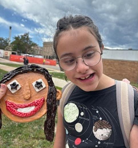 A smiling face made of clay next to a girl who is also smiling