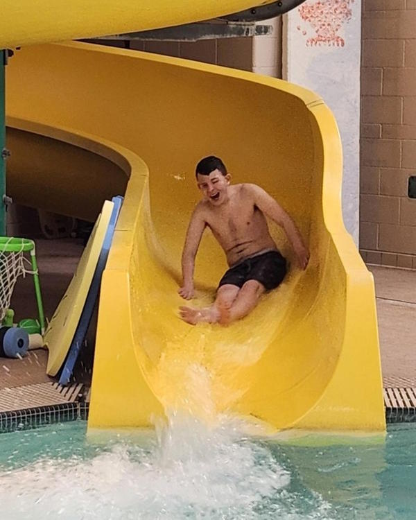 Male student rides the water slide and smiles.