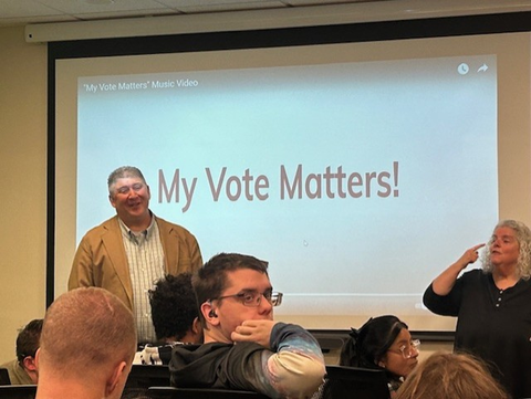 Students from BtL watch a presentation about My Vote Matters! A man presents and an interpreter signs to the students.
