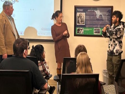 A man, student and an interpreter stand in front of group of students.