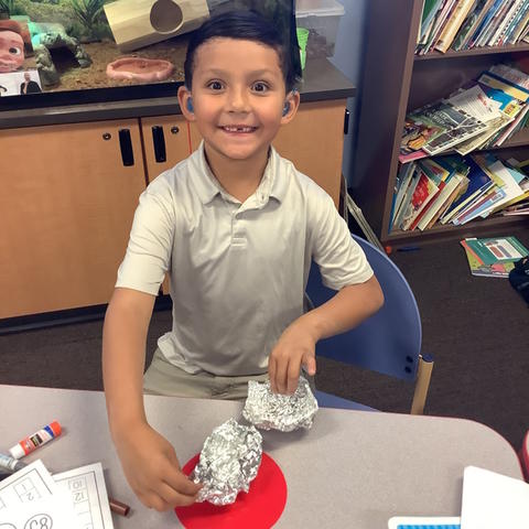 A boy smiles for the camera and holds his boat.