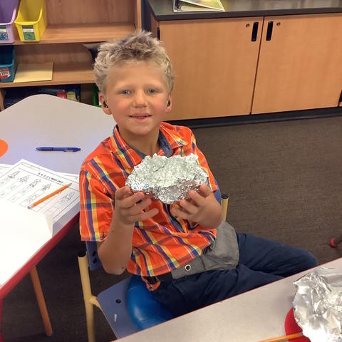  Student holding their foil boat and smiling.