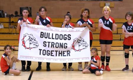 Student volleyball players hold a banner that reads Bulldogs Strong Together