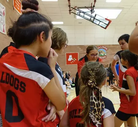 MS volleyball players circle their coach as she provides serious instruction