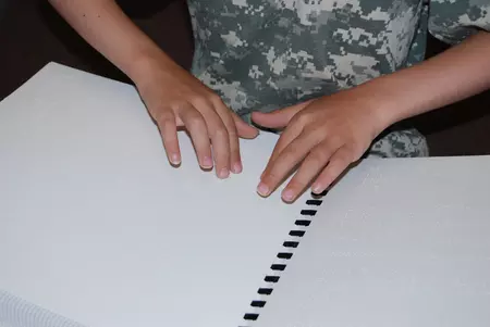 Hands reading comb-bound braille book