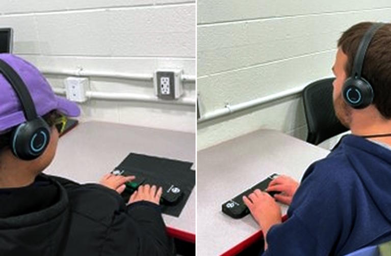 Student on the left is wearing a hat and headphones and uses the Cadence Braille Display.  The student on the right is wearing headphones and uses the braille display.