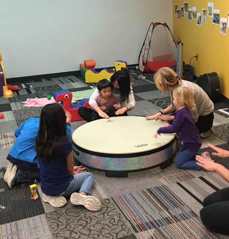Children gather around a drum with a teacher