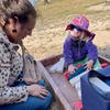 A preschool student plays with blocks while her teacher watches.]