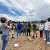 In a garden, a group of students and a dorm staff member stand in a semi circle as a dorm supervisor communicates in ASL. 