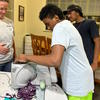  A boy shreds purple cabbage in an electric slicer while a dorm supervisor and another student watch.