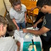  Another boy shreds cabbage in an electric slicer while a dorm supervisor and another student watch.